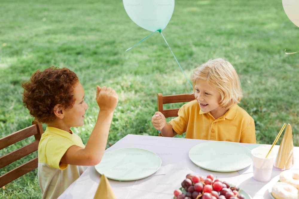 Deux enfants à la table de pique-à l’extérieur décorée de ballons pour la fête d’anniversaire en été, espace de copie