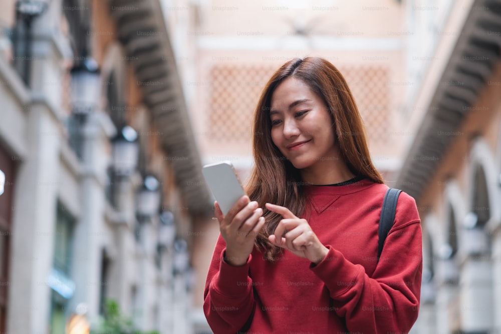 Una joven asiática sosteniendo y usando el teléfono móvil mientras viaja y hace turismo por la ciudad