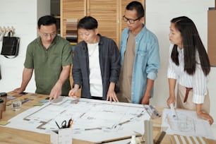 Eine Gruppe junger Architekten versammelte sich an einem Tisch mit einer großen Skizze auf dem Bauplan und diskutierte die Arbeitspunkte bei der Sitzung