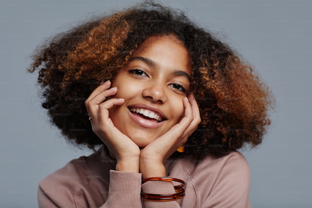 Minimal close up portrait of young African-American woman with natural curly hair smiling at camera against blue background