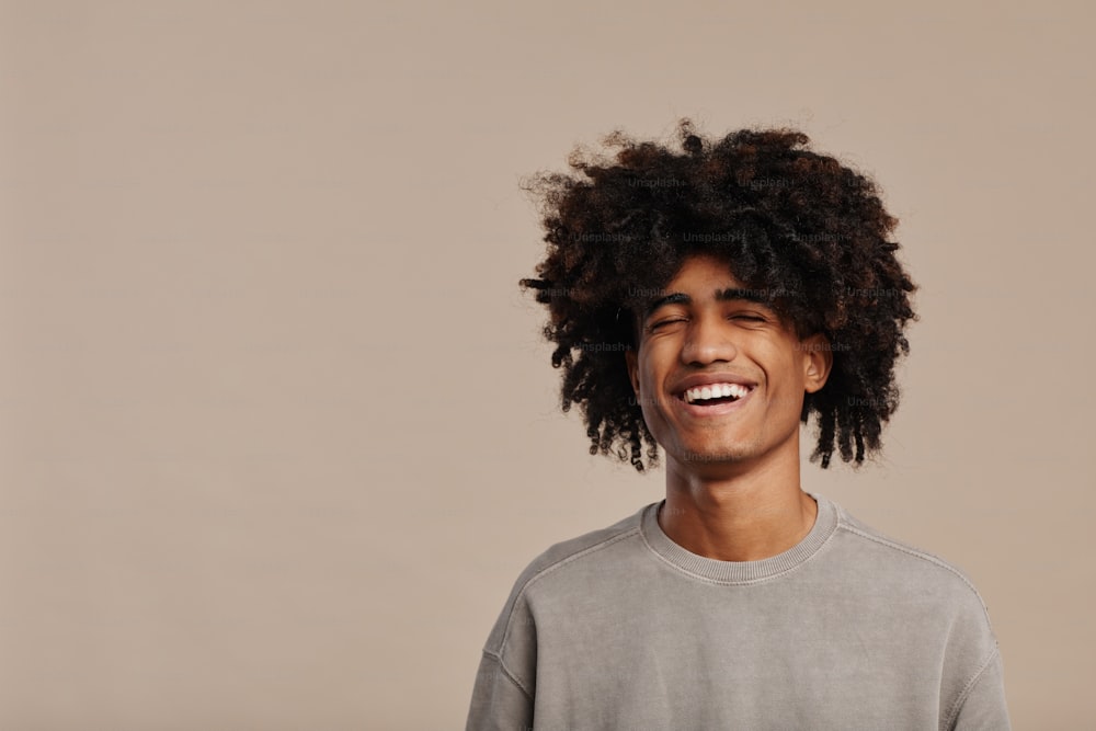 Portrait minimal d’un jeune homme afro-américain riant avec des cheveux bouclés naturels sur fond beige clair, espace de copie