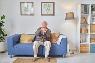 Senior man with crutch sitting and resting on the sofa in the living room