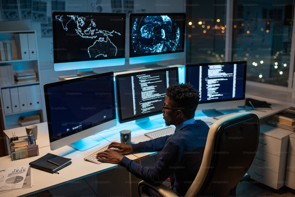 Jeune développeur de logiciels contemporain travaillant avec des données décodées assis devant un écran d’ordinateur au bureau la nuit