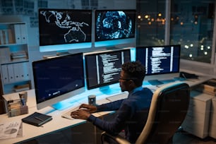 Junger zeitgenössischer Softwareentwickler, der mit dekodierten Daten arbeitet, während er nachts vor einem Computermonitor im Büro sitzt