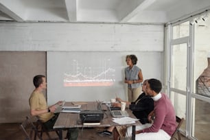 Une jeune économiste debout près d’un tableau blanc interactif avec un graphique financier tout en interagissant avec le public lors d’un séminaire d’affaires