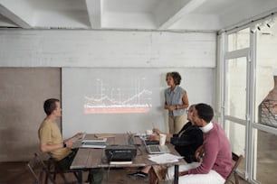 Young female economist standing by interactive whiteboard with financial graph while interacting with audience at business seminar