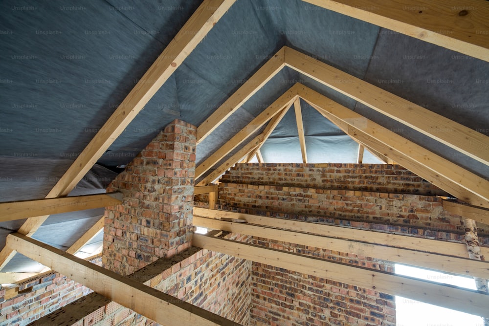 Attic space of a building under construction with wooden beams of a roof structure and brick walls. Real estate development concept.
