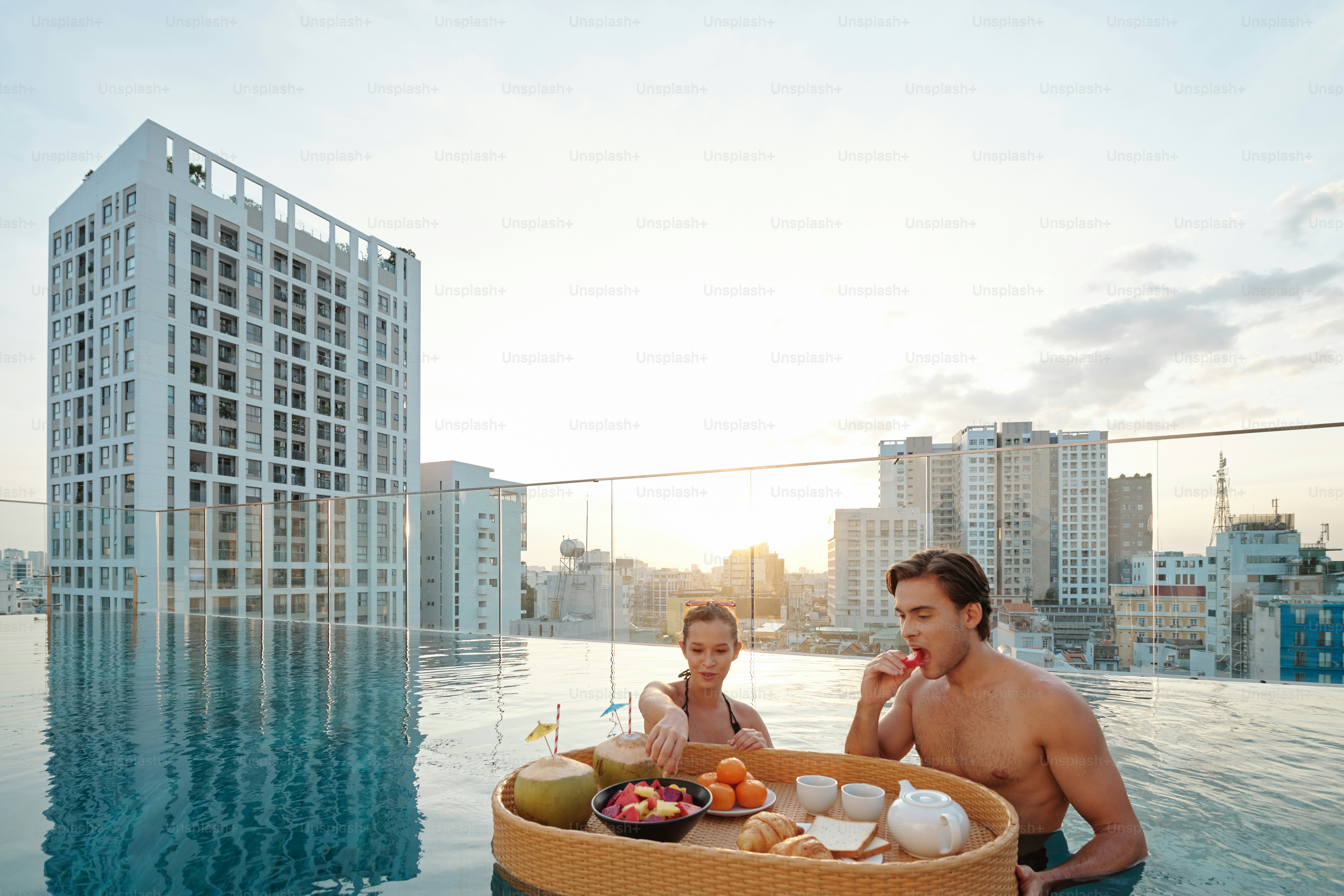 Attractive young man and woman eating delicious breakfast in rooftop swimming pool