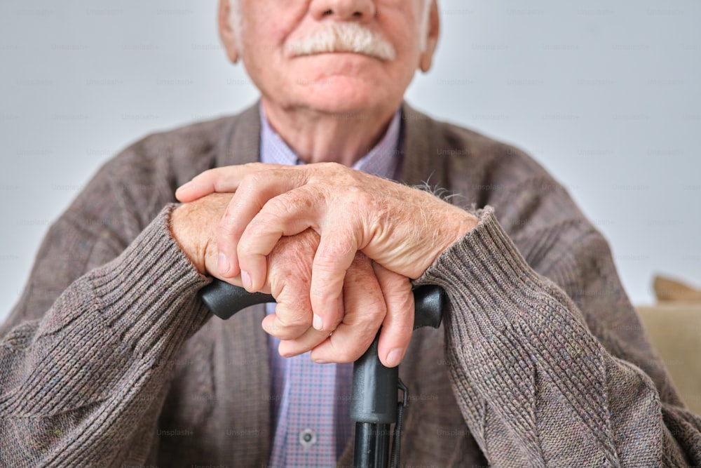 Primo piano di un uomo anziano con baffi bianchi seduto appoggiato alla sua stampella