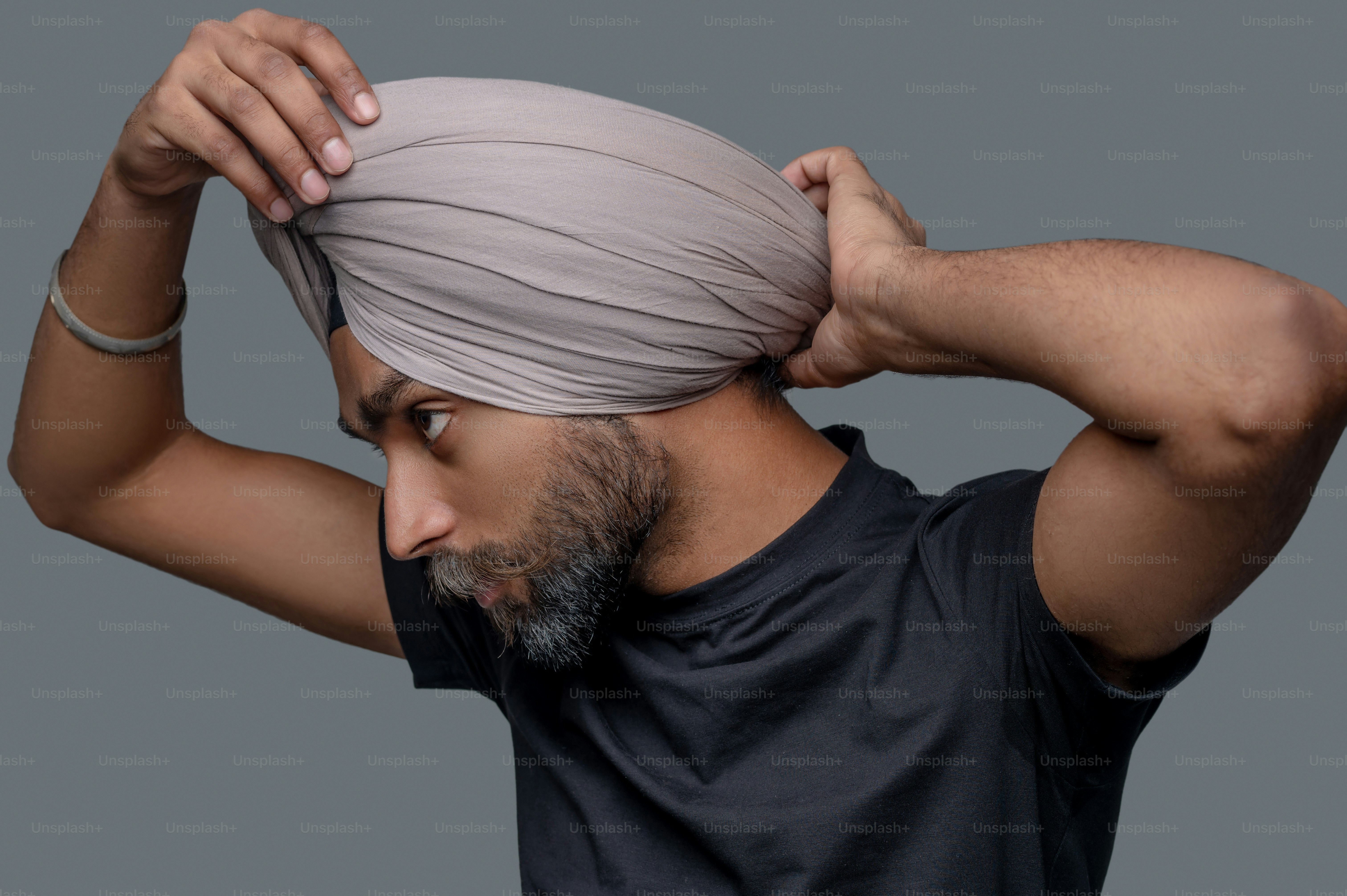 Portrait of a serious handsome bearded mustached middle-aged Indian man focused on tying his headwear