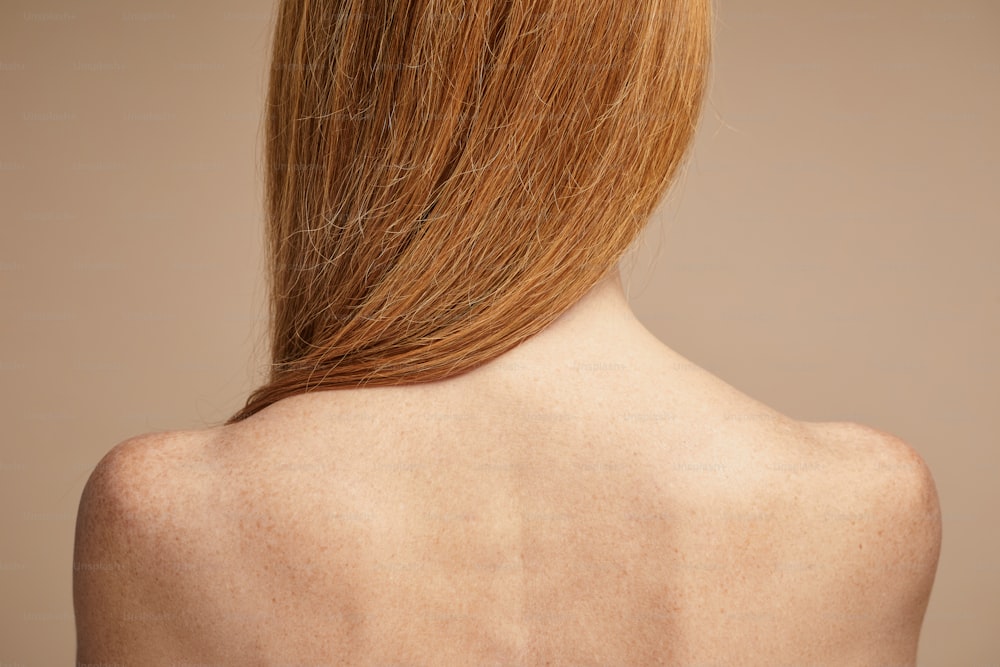 Minimal back view of freckled red haired woman with nude shoulders, copy space