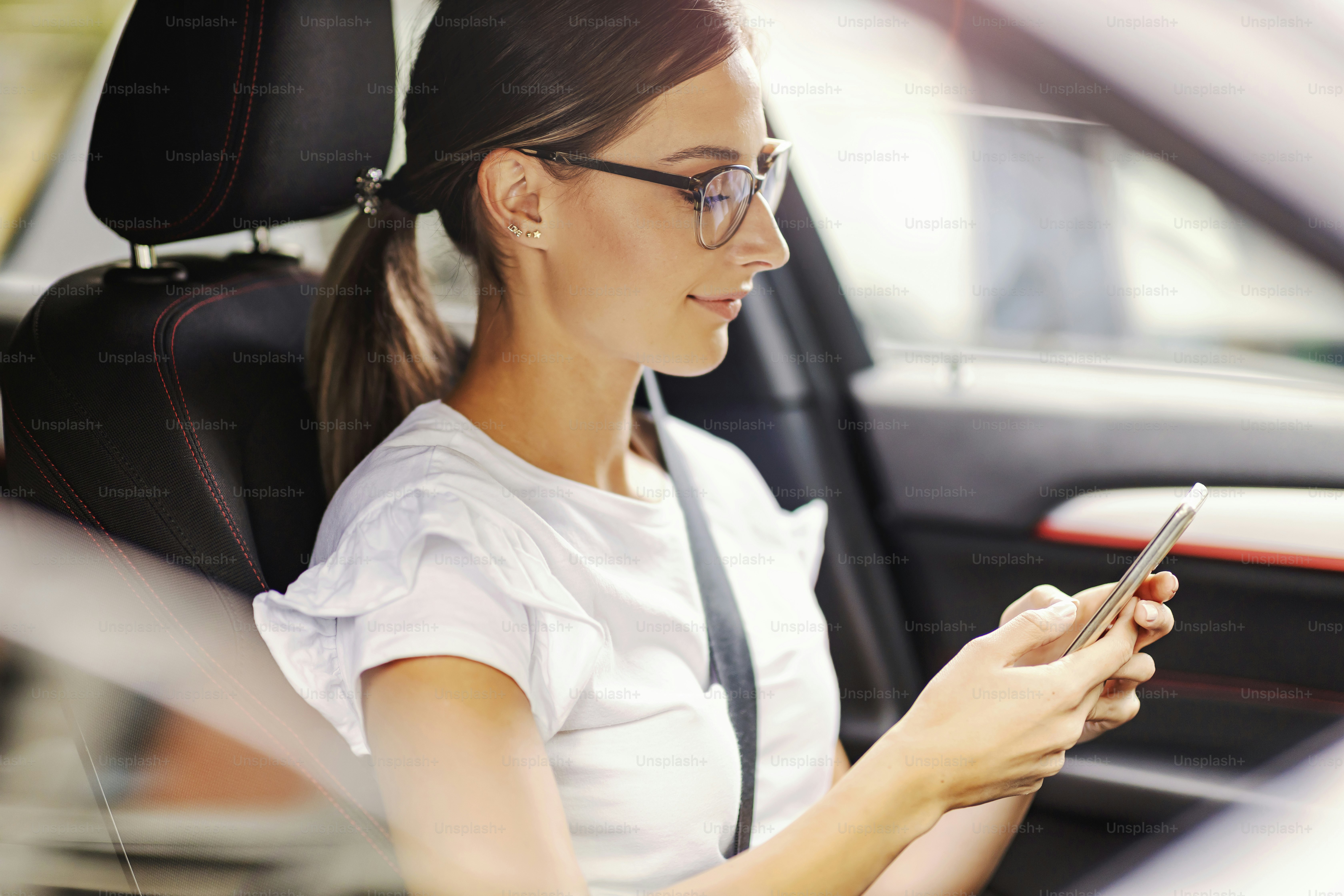A happy woman sitting in her car and texting a message. A woman in a car with a phone