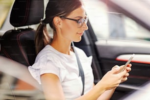 행복한 여자가 차에 앉아 메시지를 보내고 있다. 전화기를 들고 차 안에 있는 여자