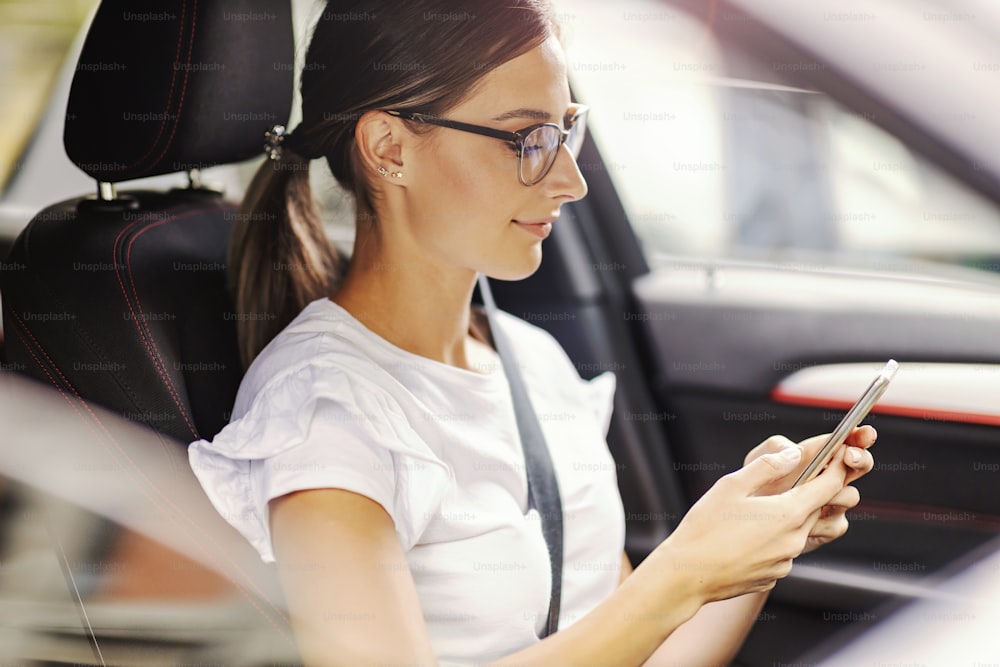 A happy woman sitting in her car and texting a message. A woman in a car with a phone