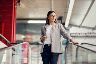 A young, elegant businesswoman descending the escalator and going into the underground garage. She is holding a phone and looking away. A workday of a businesswoman