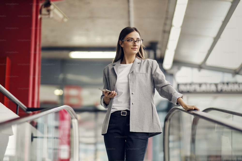 Una giovane ed elegante donna d'affari scende dalla scala mobile e va nel garage sotterraneo. Ha in mano un telefono e distoglie lo sguardo. Una giornata lavorativa di una donna d'affari