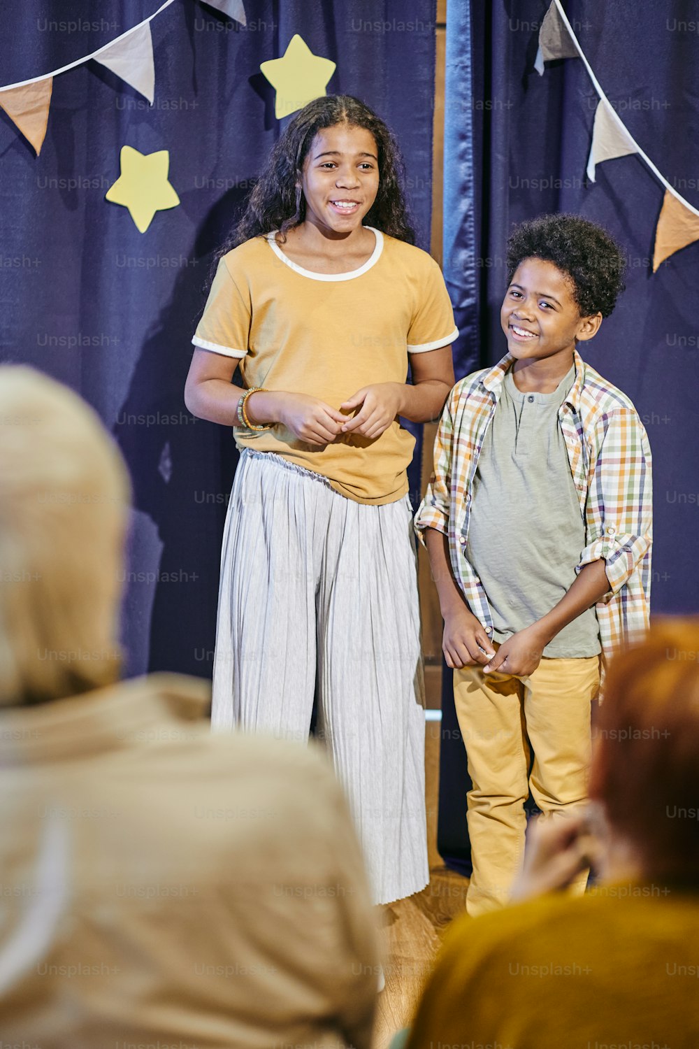 Happy siblings in casualwear performing on stage against blue curtains decorated with stars and flags