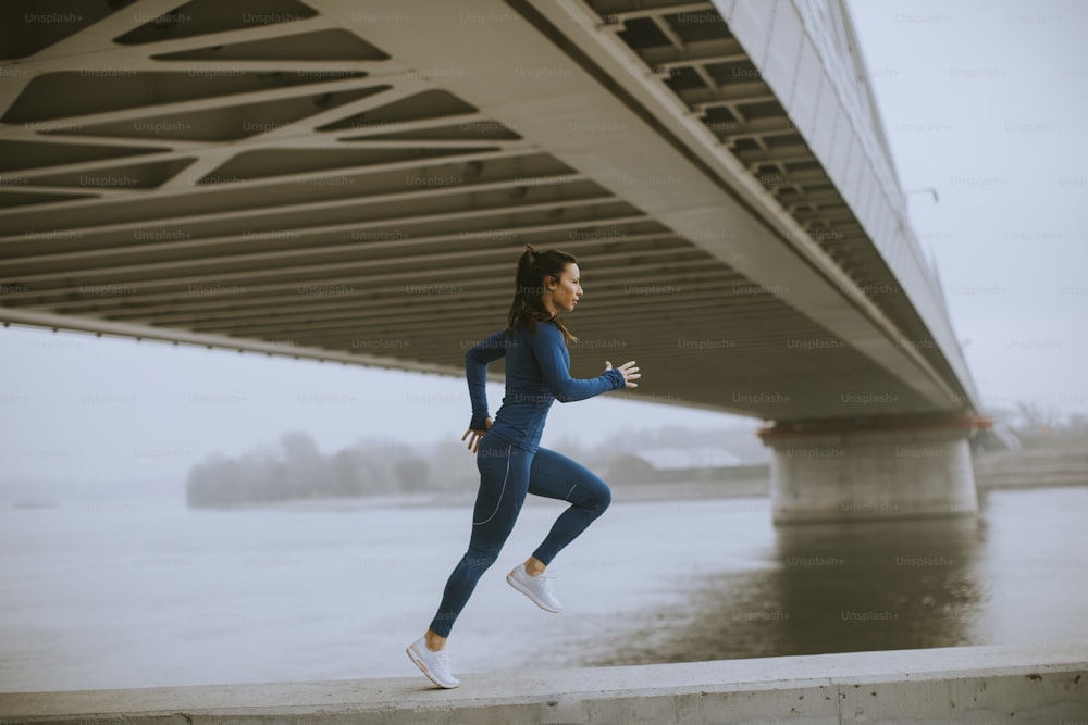 Giovane donna graziosa in tuta da ginnastica blu che corre dal fiume alla mattina d'autunno