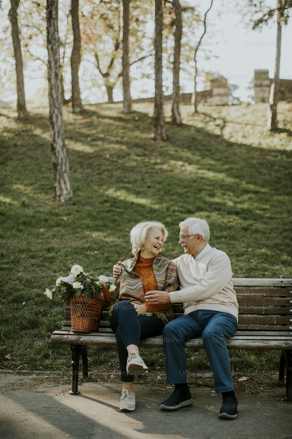花でいっぱいのバスケットを持ってベンチに座って抱きしめるハンサムな老夫婦