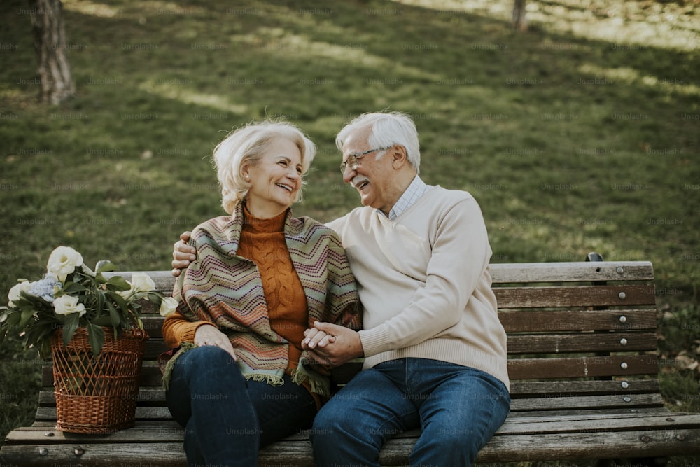 Handsome senior couple sitting on the bench with basket full of flowers and embracing