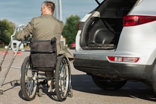 Vista trasera de un hombre adulto que usa el automóvil en silla de ruedas descargando el automóvil en el estacionamiento al aire libre, copie el espacio