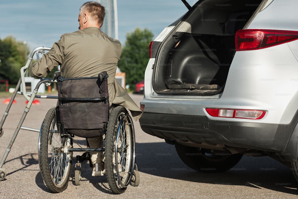 야외 주차장에서 휠체어를 타고 차를 내리는 성인 남성의 뒷모습, 복사 공간