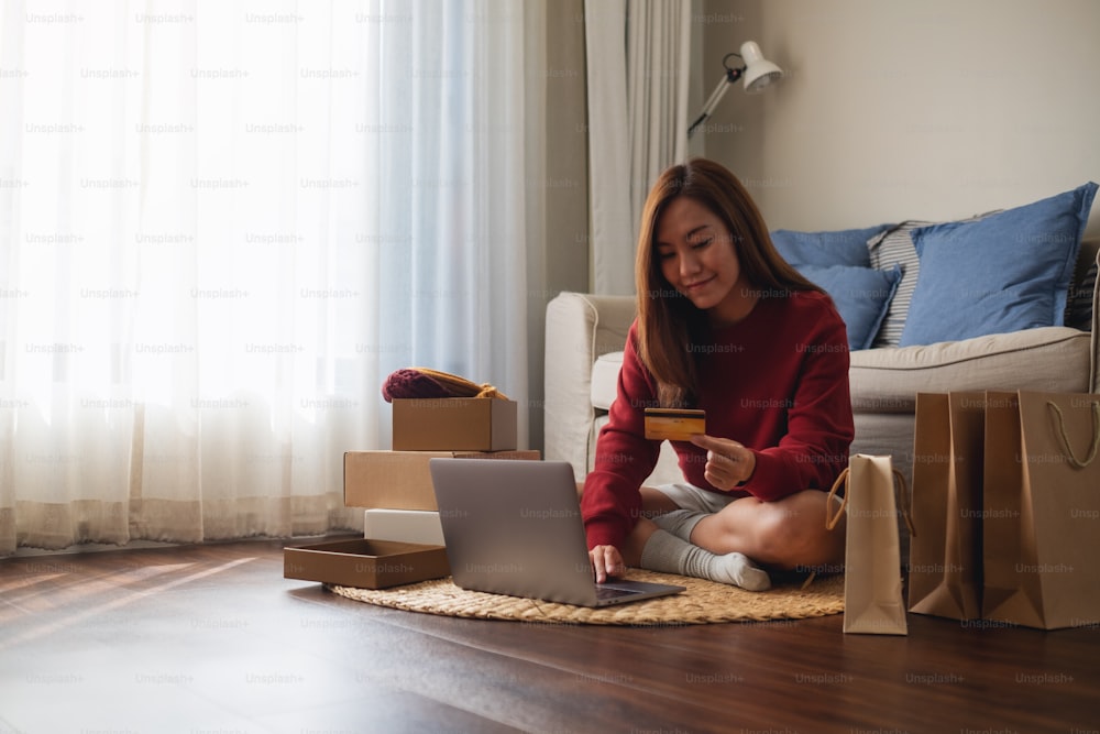 Uma mulher usando computador portátil e cartão de crédito para compras on-line em casa