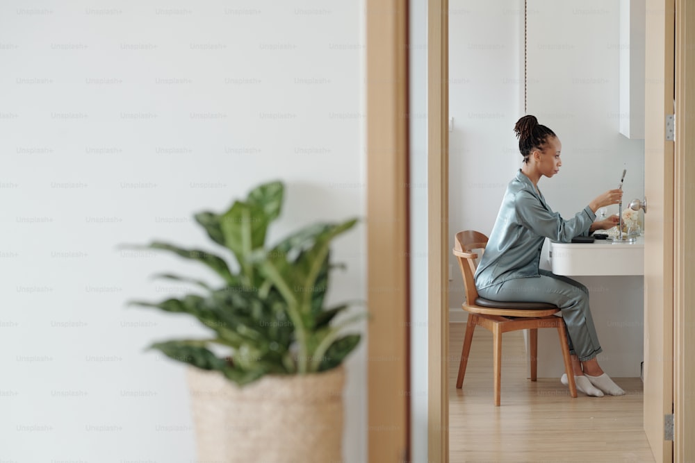 Hermosa mujer en ropa de salón colocando espejo de aumento en el tocador en su habitación