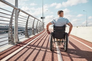 Back view portrait of man in wheelchair in accessible city environment outdoors lit by sunlight, copy space