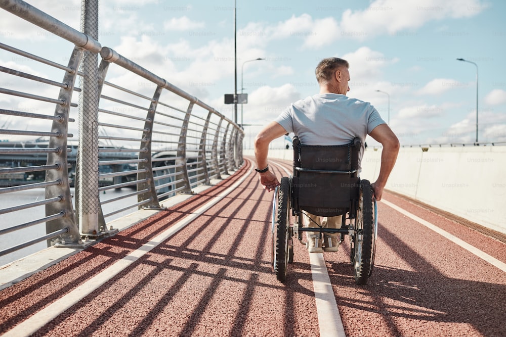 Back view portrait of man in wheelchair in accessible city environment outdoors lit by sunlight, copy space