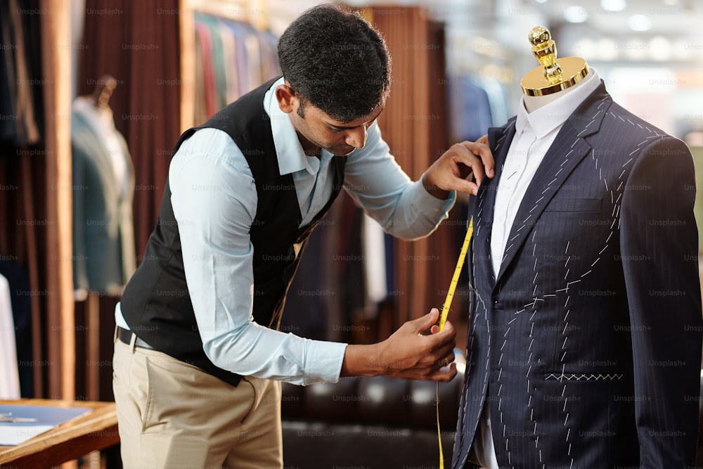 Jovem alfaiate criativo medindo jaqueta sob medida no manequim em que está trabalhando