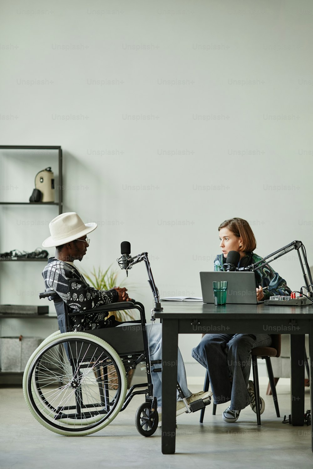 Vertical full length portrait of African-American person with disability speaking to microphone while recording podcast in studio