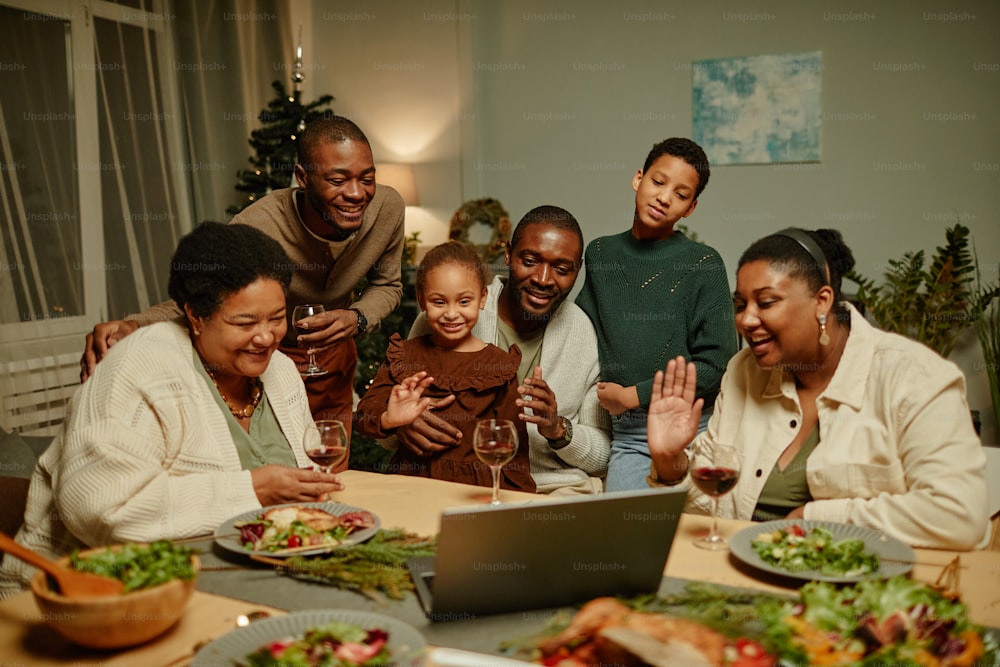 Retrato de una gran familia afroamericana saludando a la cámara mientras conversa por video con amigos en la cena de Navidad