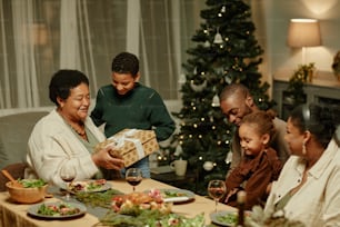 Portrait d’une grand-mère afro-américaine heureuse ouvrant un cadeau tout en profitant de Noël en famille