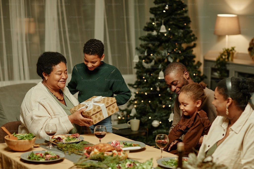 Portrait of happy African-American grandmother opening present while enjoying Christmas with family