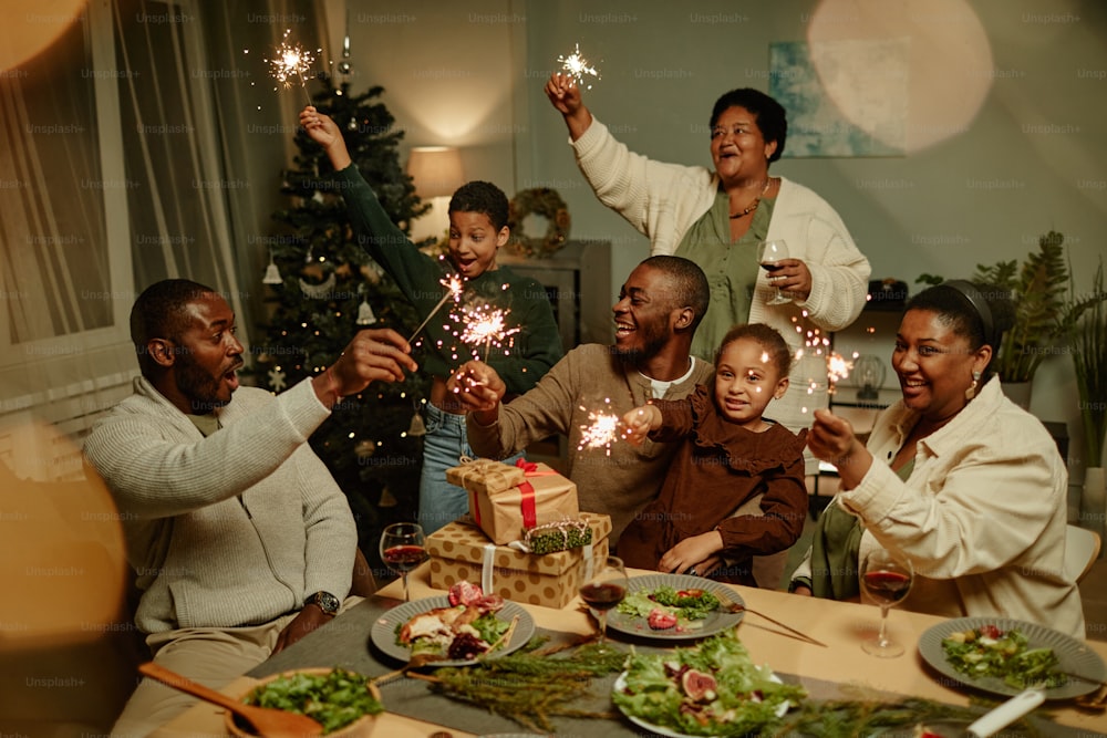 Porträt einer glücklichen afroamerikanischen Familie, die Wunderkerzen anzündet, während sie gemeinsam Weihnachten zu Hause genießt