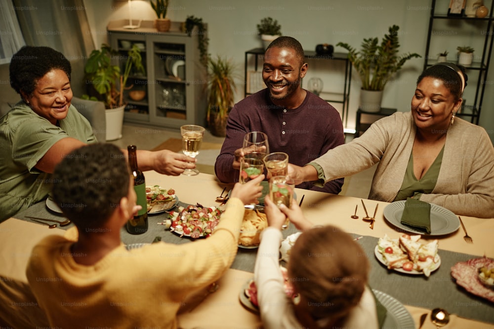 High angle portrait of happy African-American family clinking glasses while enjoying dinner party at home
