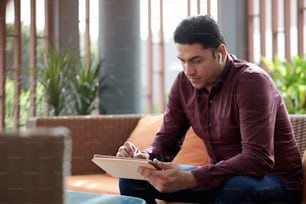 Serious businessman signing document on tablet computer or filling form with personal data