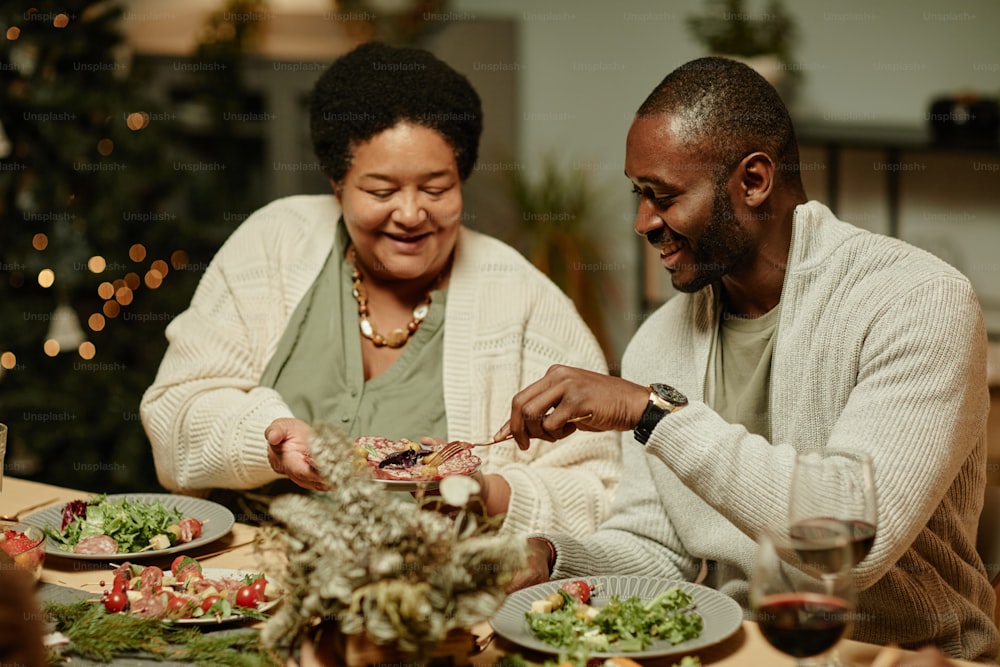 Portrait of smiling African-American grandmother serving food while celebrating Thanksgiving with family at dinner table