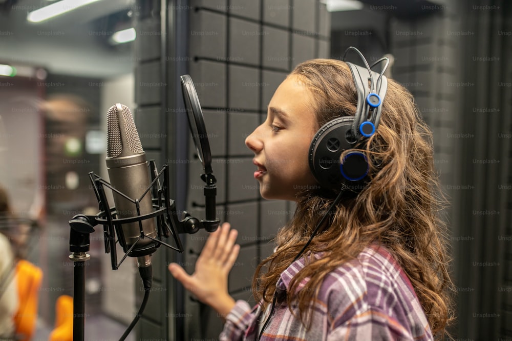 Vista lateral de uma jovem caucasiana serena nos fones de ouvido assinando no microfone