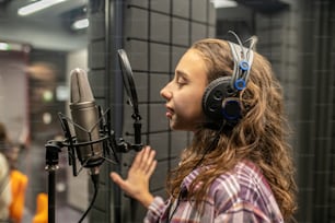 Vista lateral de uma jovem caucasiana serena nos fones de ouvido assinando no microfone