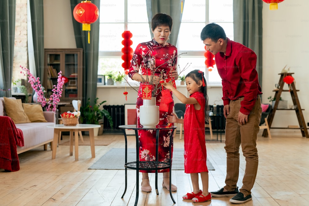 Family of three decorating branches with postcards containing best wishes for holiday while preparing for chinese new year