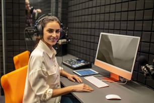 Ritratto in vita di una giovane donna allegra in cuffia in posa per la telecamera nello studio di registrazione