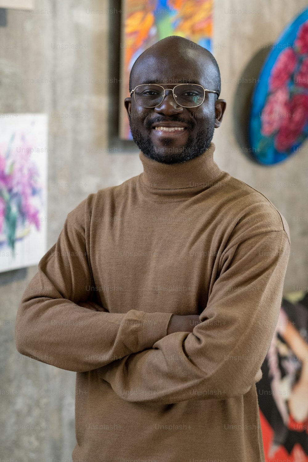 Portrait of African young man standing with arms crossed and looking at camera while standing in art gallery