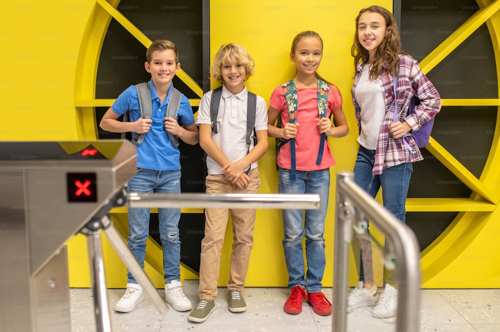 Full-length portrait of four cute cheerful kids in casual clothes posing for the camera in the lobby of a recording studio