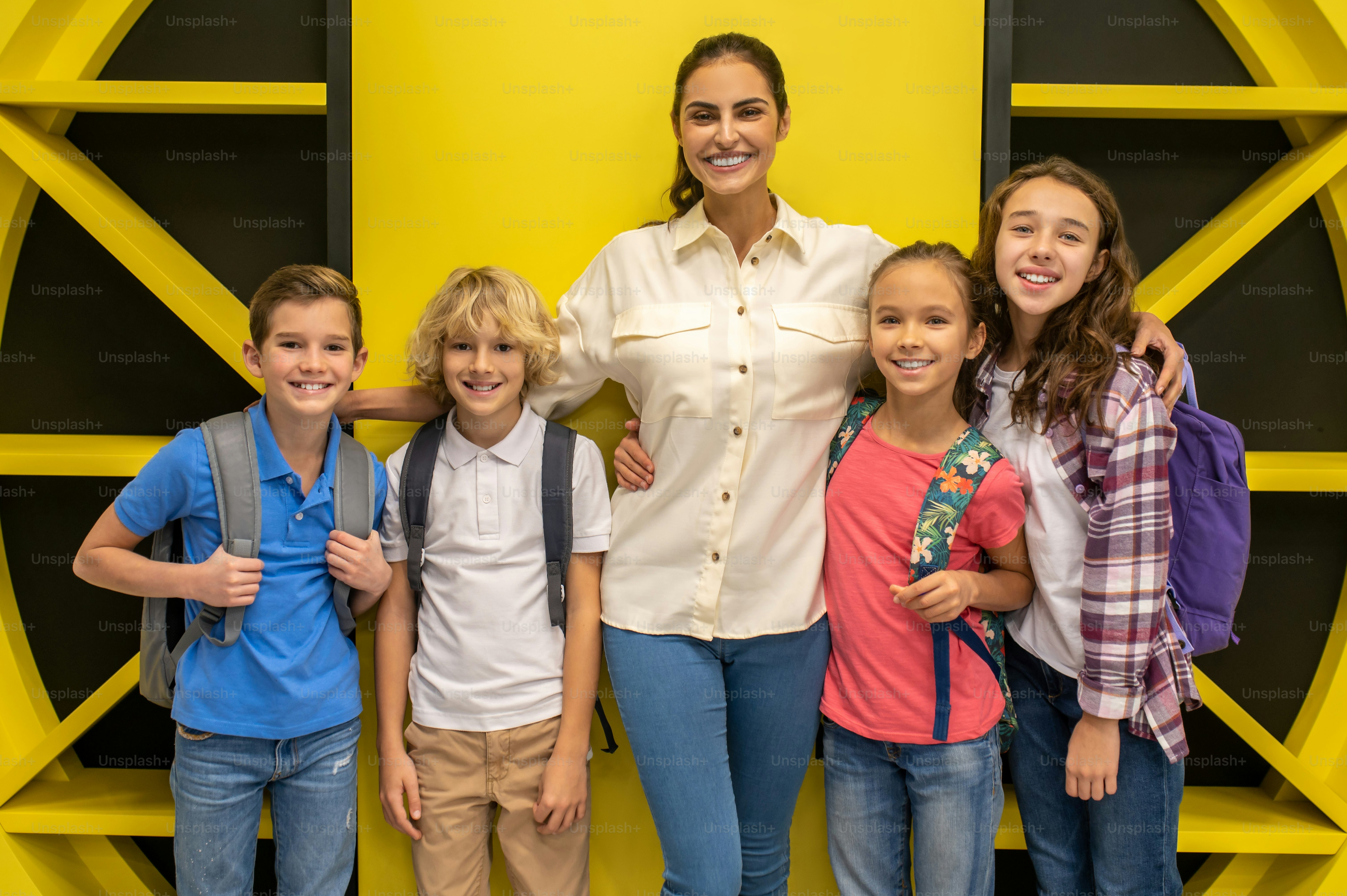 Front view of a cheerful female teacher hugging her joyous schoolchildren during the photo shoot