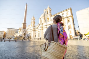 Mulher caminha na praça Navona, na cidade de Roma, em um dia ensolarado. Pessoa feminina com bolsa e xale colorido no cabelo. Conceito de estilo de vida italiano e viagens