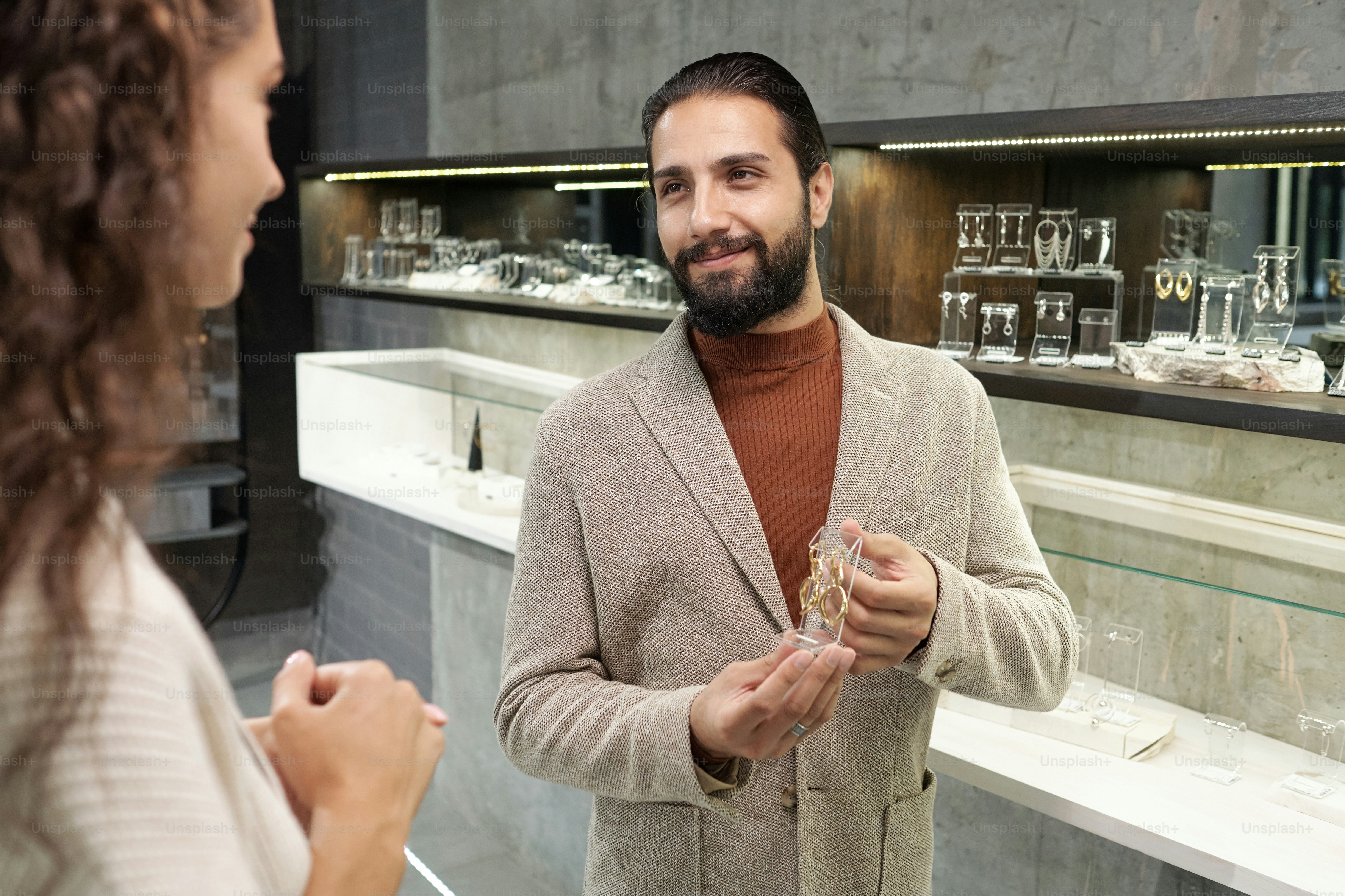 Happy young man and his girlfriend choosing new earrings while visiting large jewelry boutique in department store