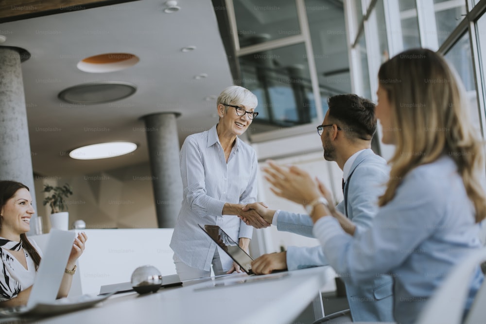 Mature business woman handshaking with young colleague on a meeting in the office