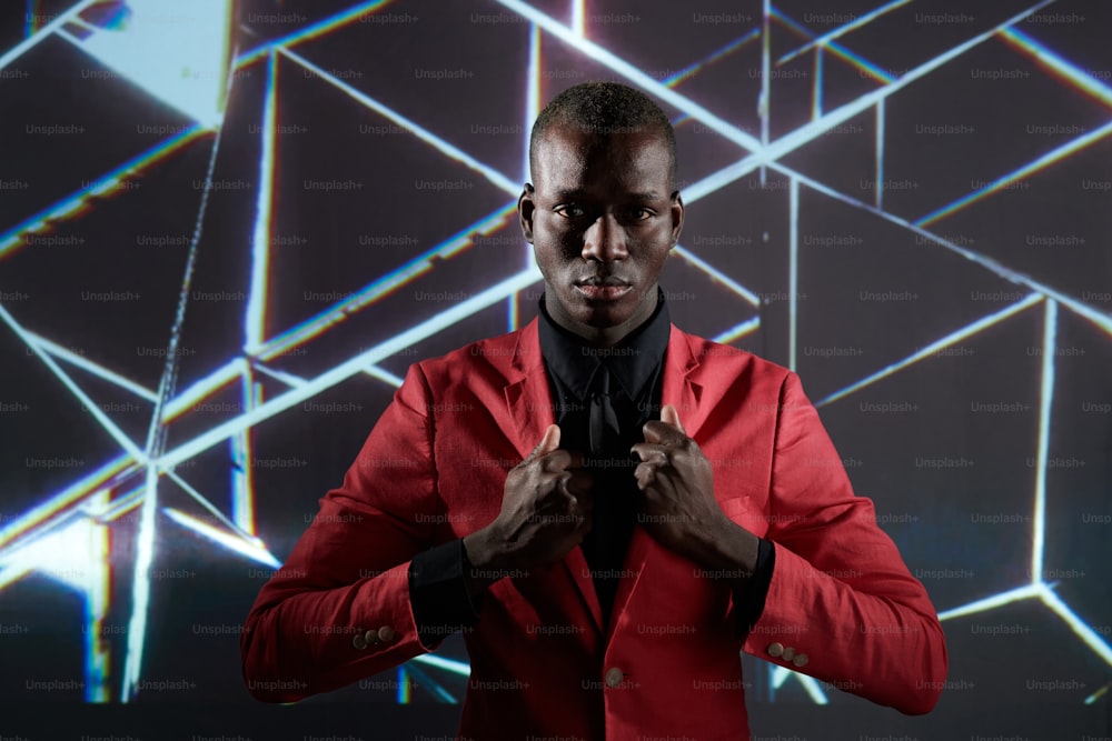 Junger ernster afrikanischer Mann in schwarzem Hemd und Krawatte und purpurroter Jacke, der mit kreativem Muster an der Wand steht